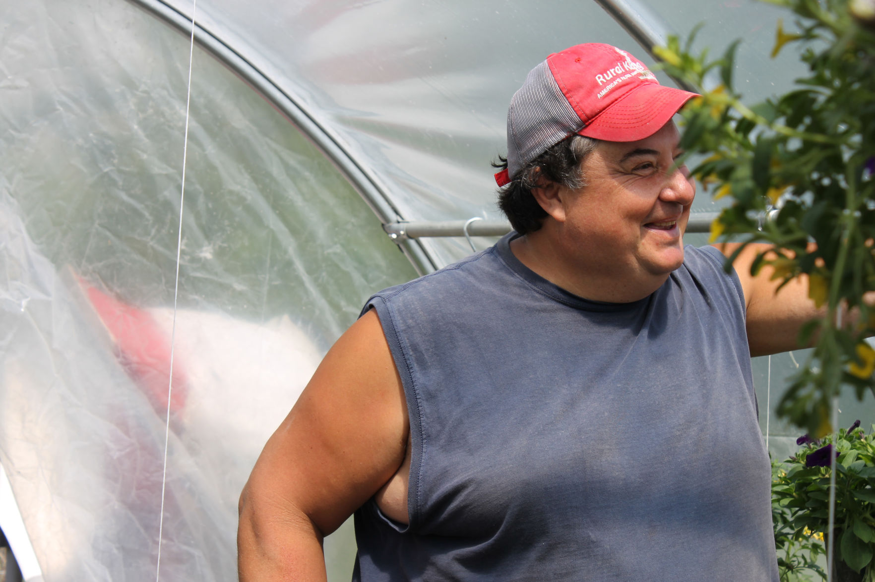 David Ybarra grins near a hanging flower basket within his farm's high tunnel